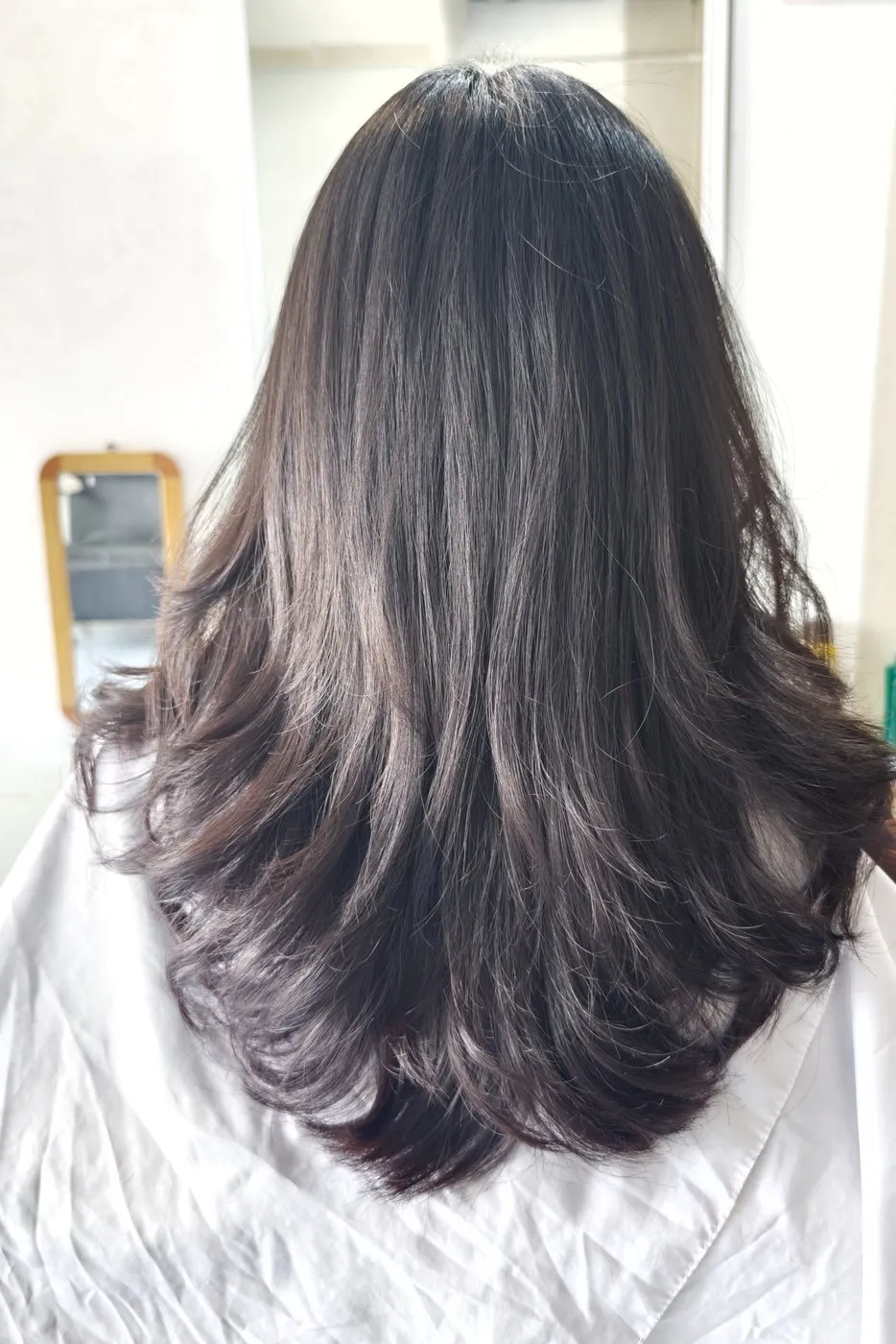 ผมยาวสีเข้มซอยเป็นชั้น ปลายผมม้วนเป็นลอนนุ่ม มองจากด้านหลัง